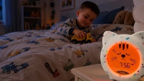 A young child in bed, playing with a toy truck while the Kip the Kitty clock indicates it's time to sleep.